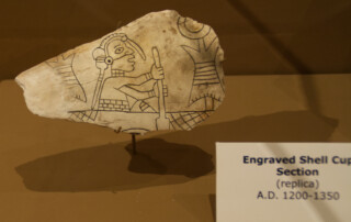 Replica of a design carved into a shell showing a man paddling a canoe